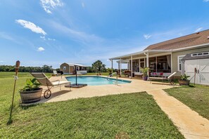 A backyard with a swimming pool, covered patio, and lawn chairs.