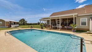 A swimming pool with a covered patio area, a lawn, and a house in the background. - BBQ Ready: Farm-style Kinston Hideaway w/ Pool (Samson)