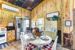 A rustic kitchen with wooden walls, a stainless steel refrigerator, a microwave, and a dining table set for four with floral centerpieces.
