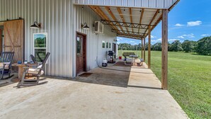 A covered outdoor area with a concrete floor, a wooden deck, and a metal building with windows and doors. - BBQ Ready: Farm-style Kinston Hideaway w/ Pool (Samson)