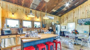 A rustic kitchen with wooden walls, a large island with stools, and a dining area with chairs. - BBQ Ready: Farm-style Kinston Hideaway w/ Pool (Samson)