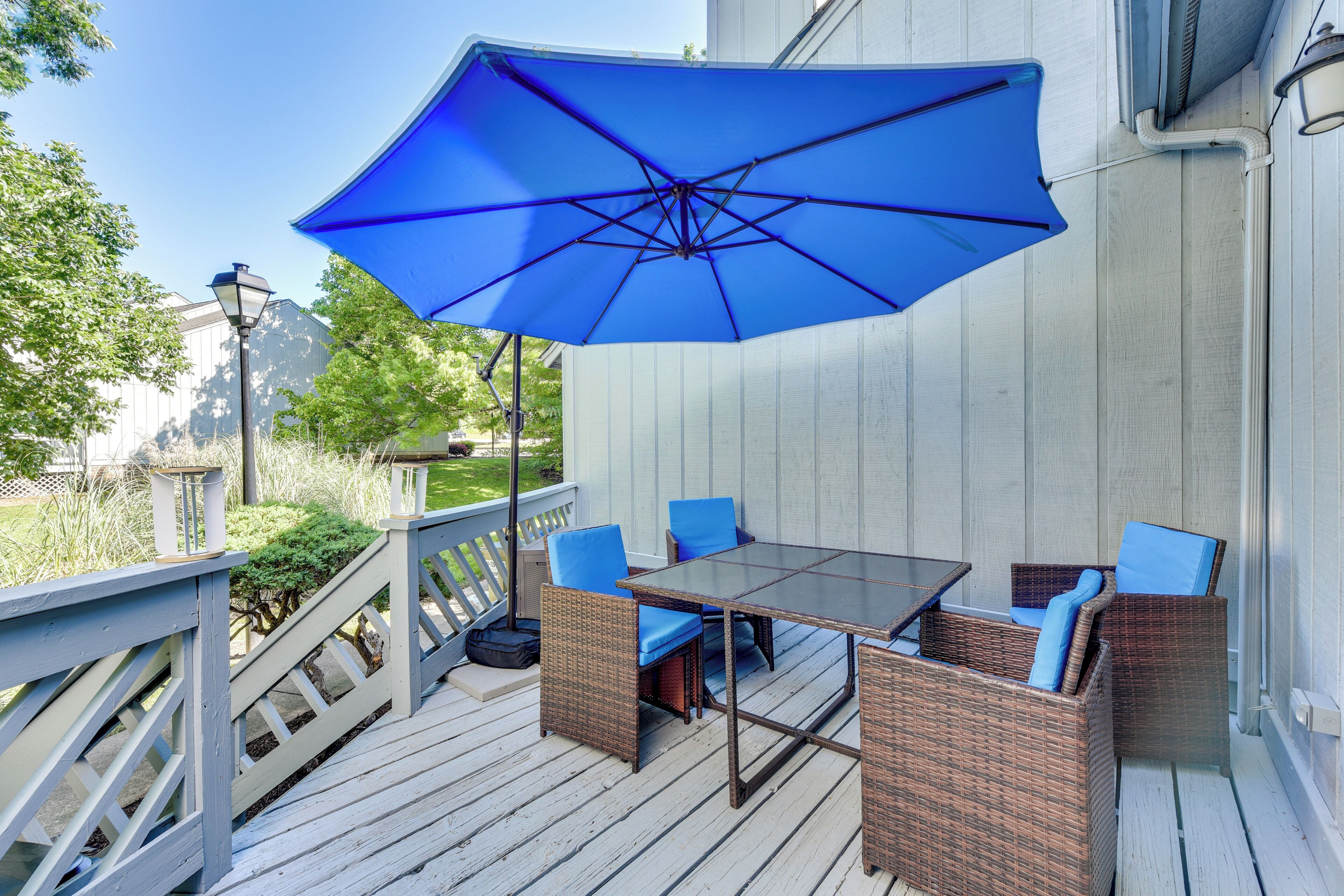 Un espace extérieur abrité, aménagé avec des meubles en osier et agrémenté d’un parasol bleu.