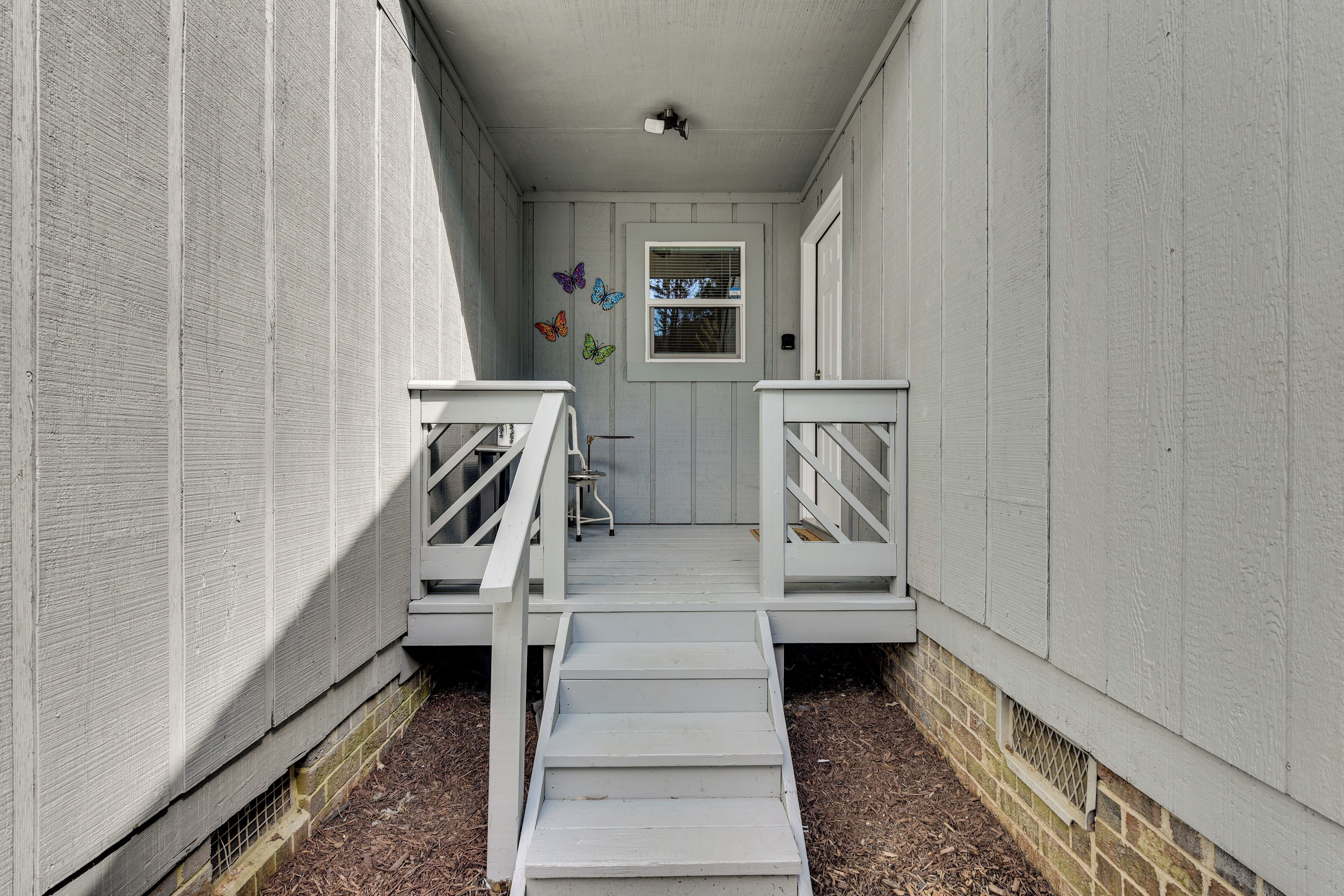 A narrow outdoor corridor with white railings and a small window with shutters.