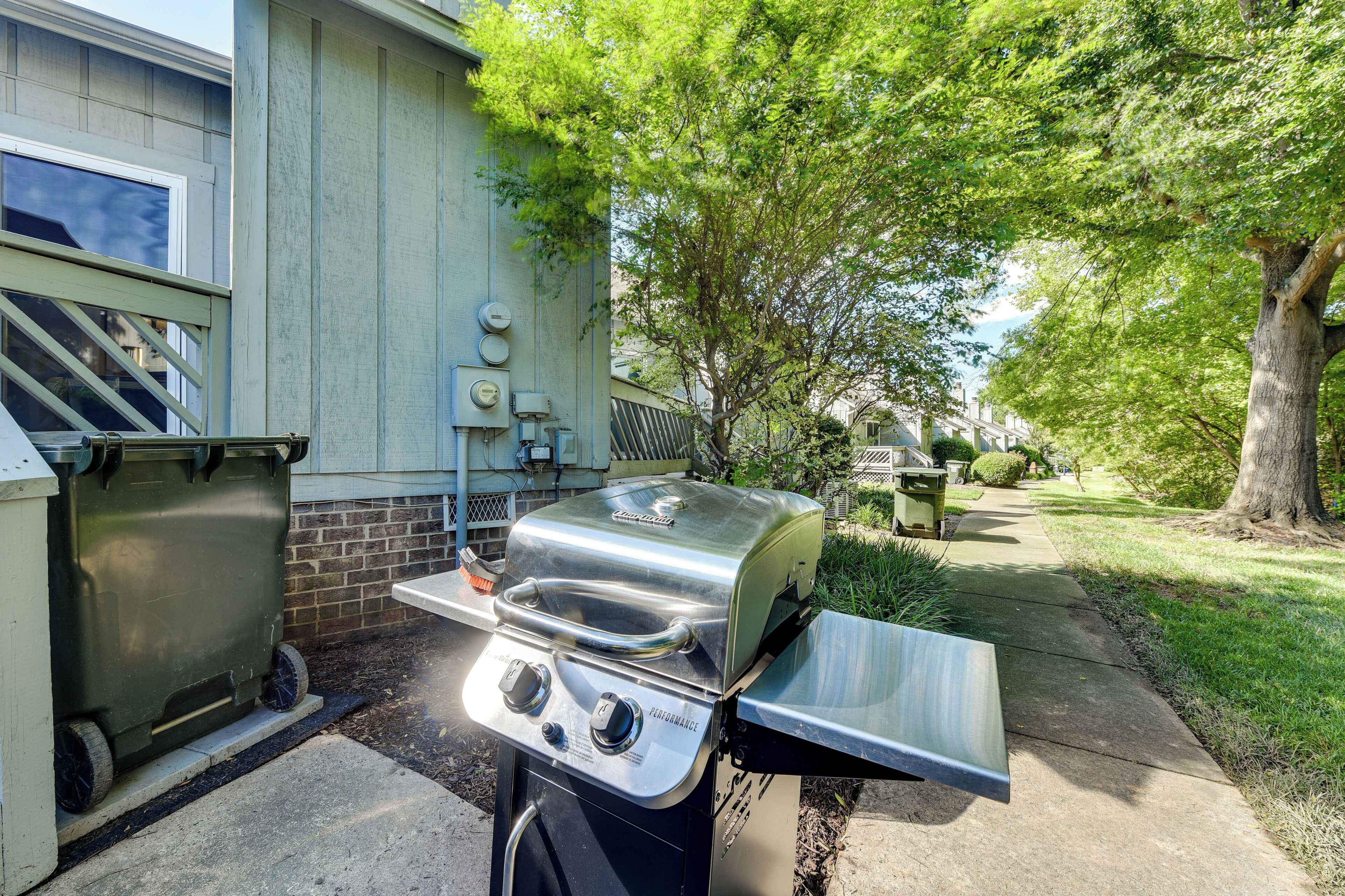 Un jardin avec un barbecue en acier inoxydable, une poubelle et un mur en briques.
