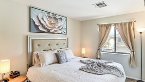 A neatly made bed with a tufted headboard, a bedside table with a lamp, and a large floral artwork above the bed. - North Las Vegas Home w/ Hot Tub - 14 Mi to Strip! (North Las Vegas)