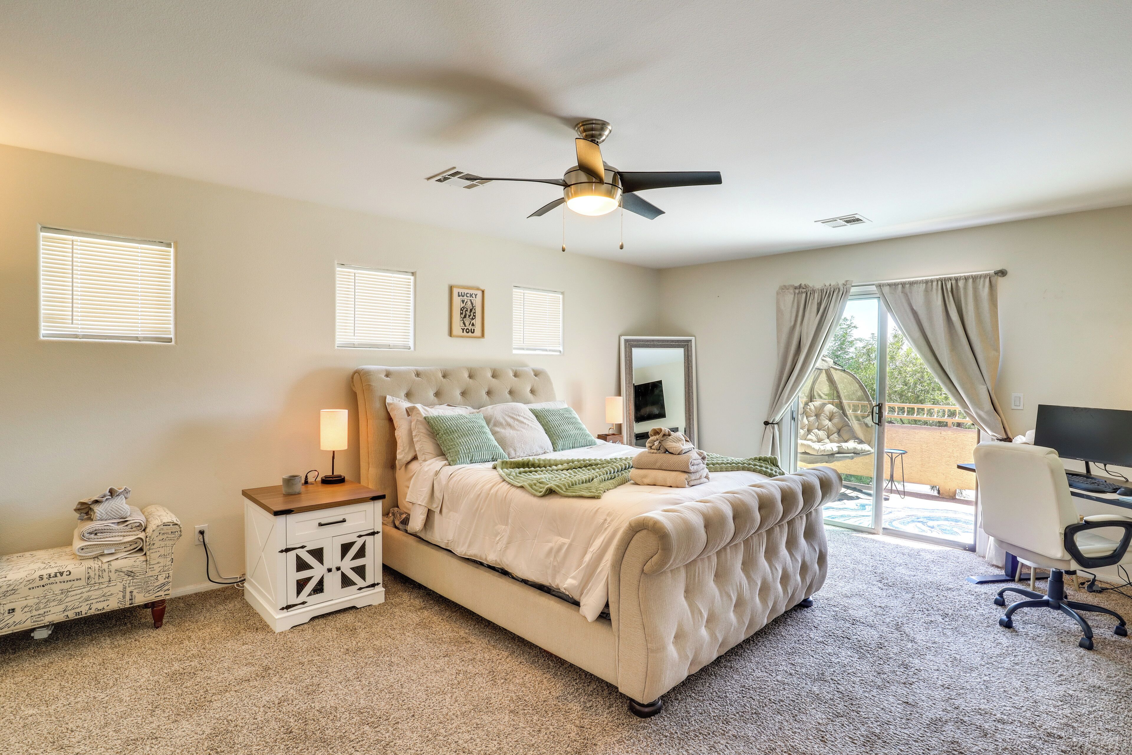 A bedroom with a bed, a desk, a chair, a ceiling fan, and a view of the outdoors.