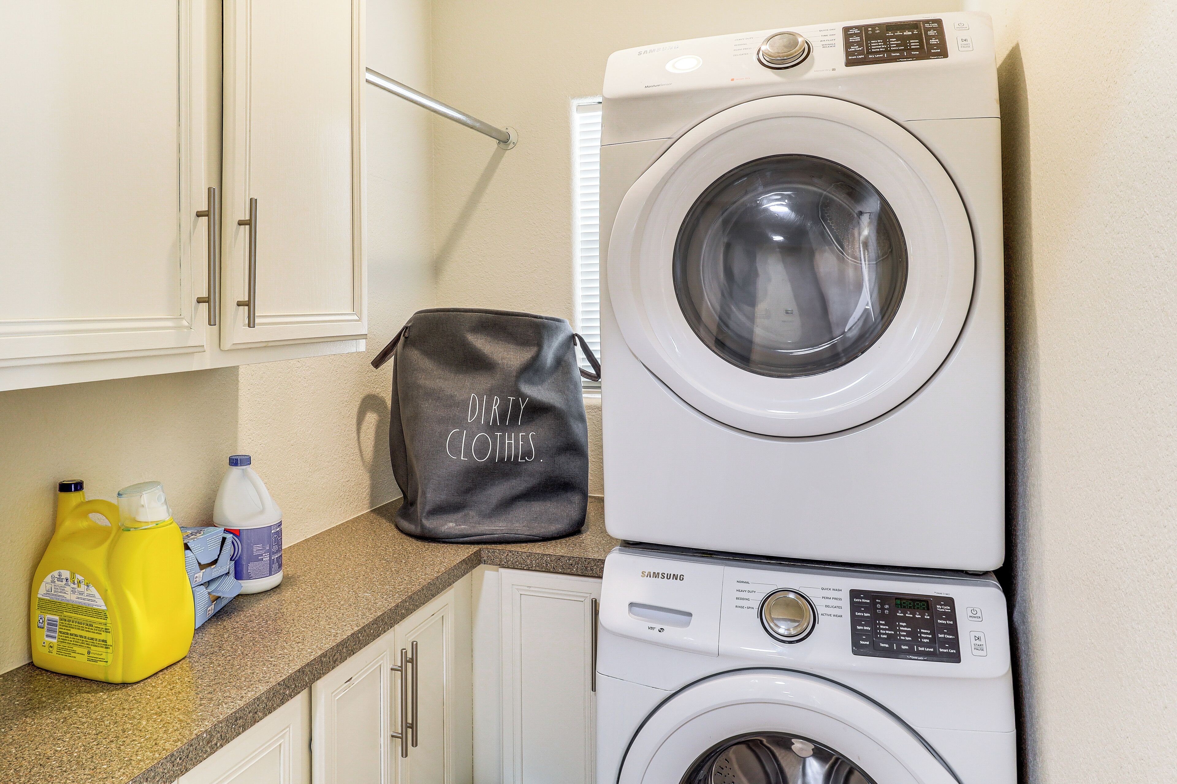 A laundry area with stacked washing machines, a detergent bottle, and a bag labeled "DIRTY CLOTHES."