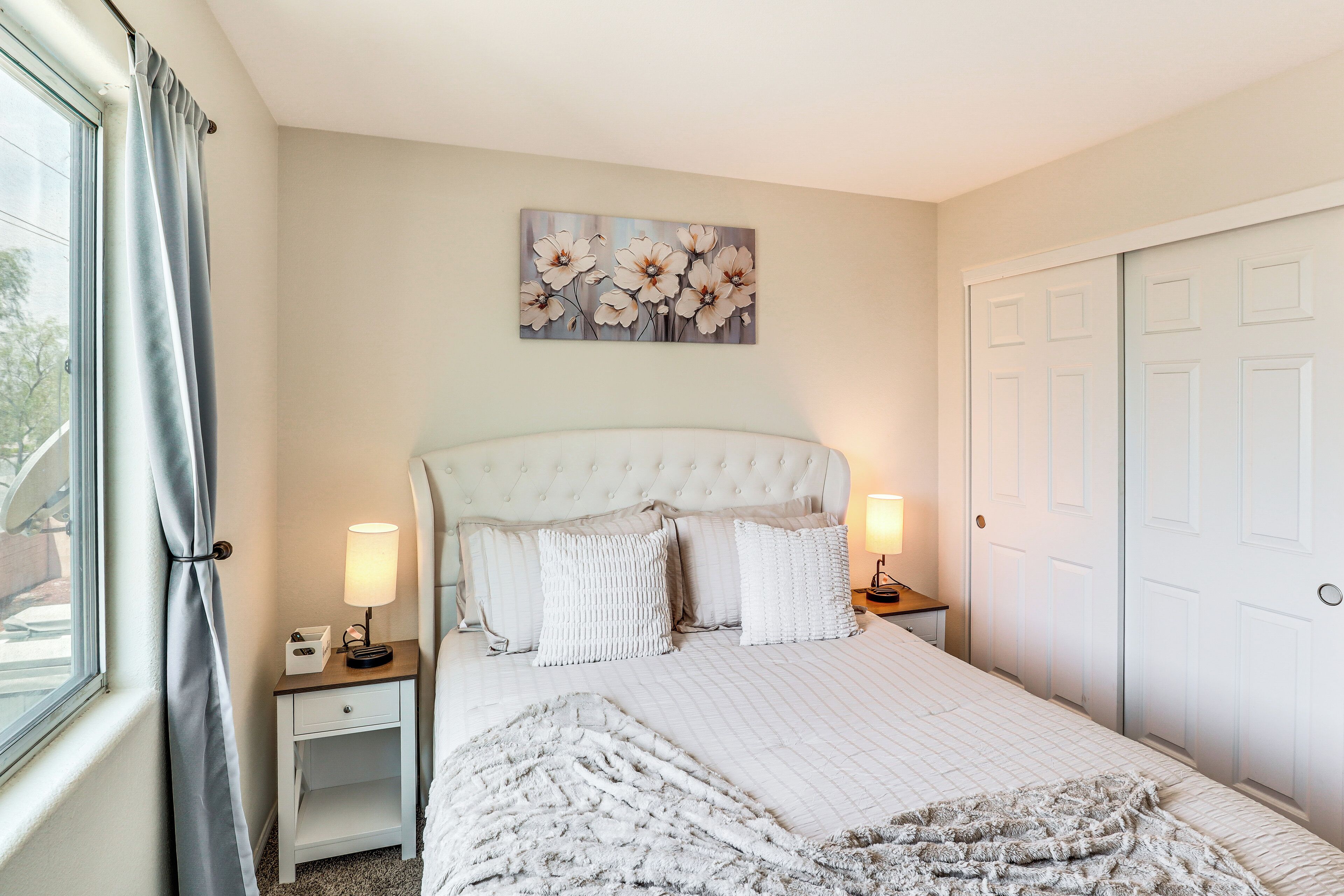 A bedroom with a large bed, two bedside tables with lamps, a wall-mounted artwork, and a closet.