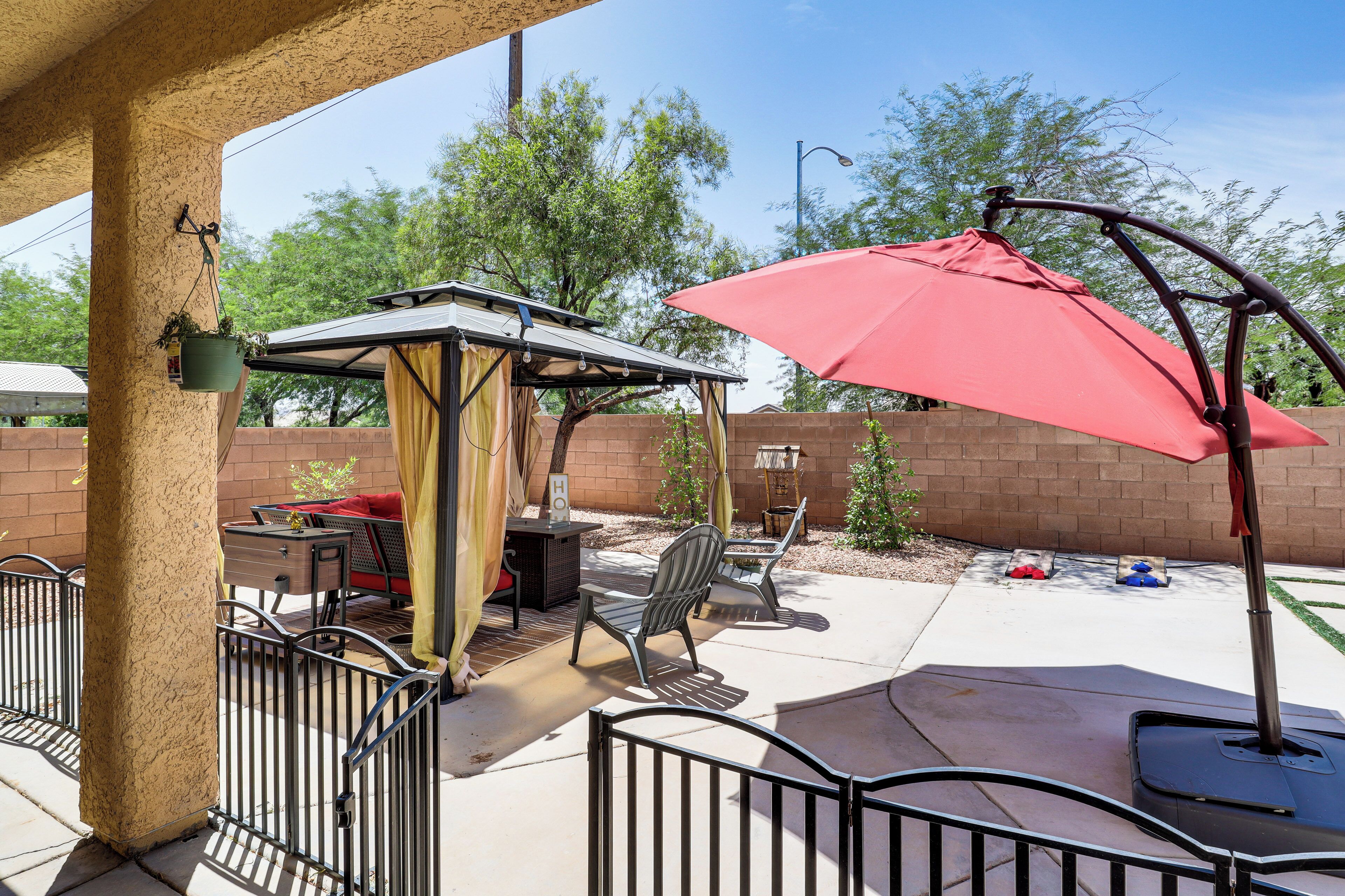 Un espace extérieur aménagé en patio, avec un coin salon couvert, un parasol rouge et une balançoire.