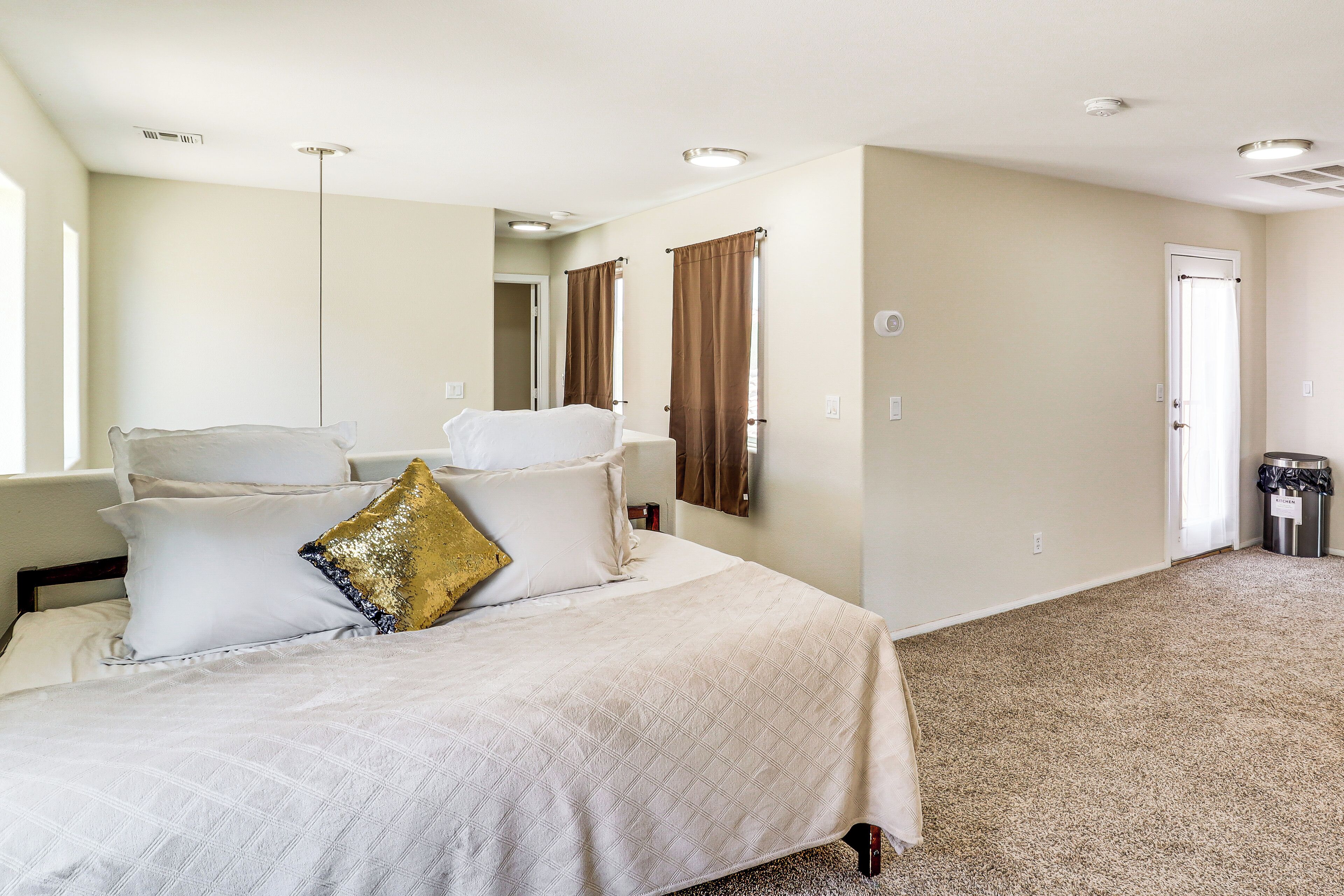 A hotel room with a large bed, a mirror, a door, and a trash bin.