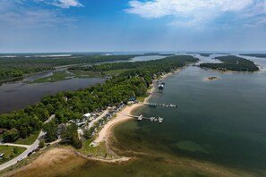 An aerial view of a coastal area with a dock, a road, and a cluster of houses along the shoreline. - Boat Rentals, Sand Beach! Les Cheneaux Islands Gem (Cedarville)