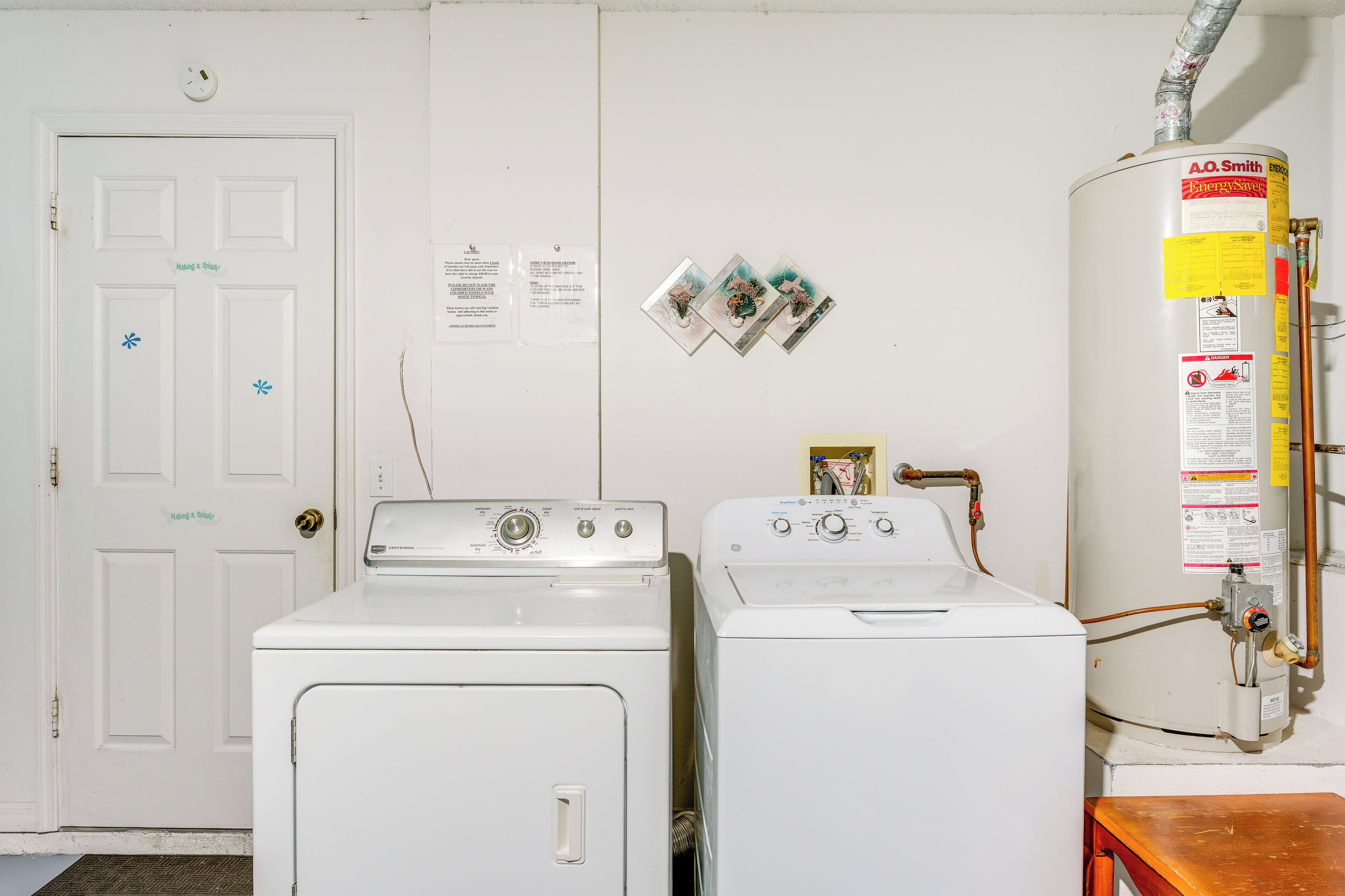 Een wasruimte met twee witte wasmachines, een boiler en een deur met slot.