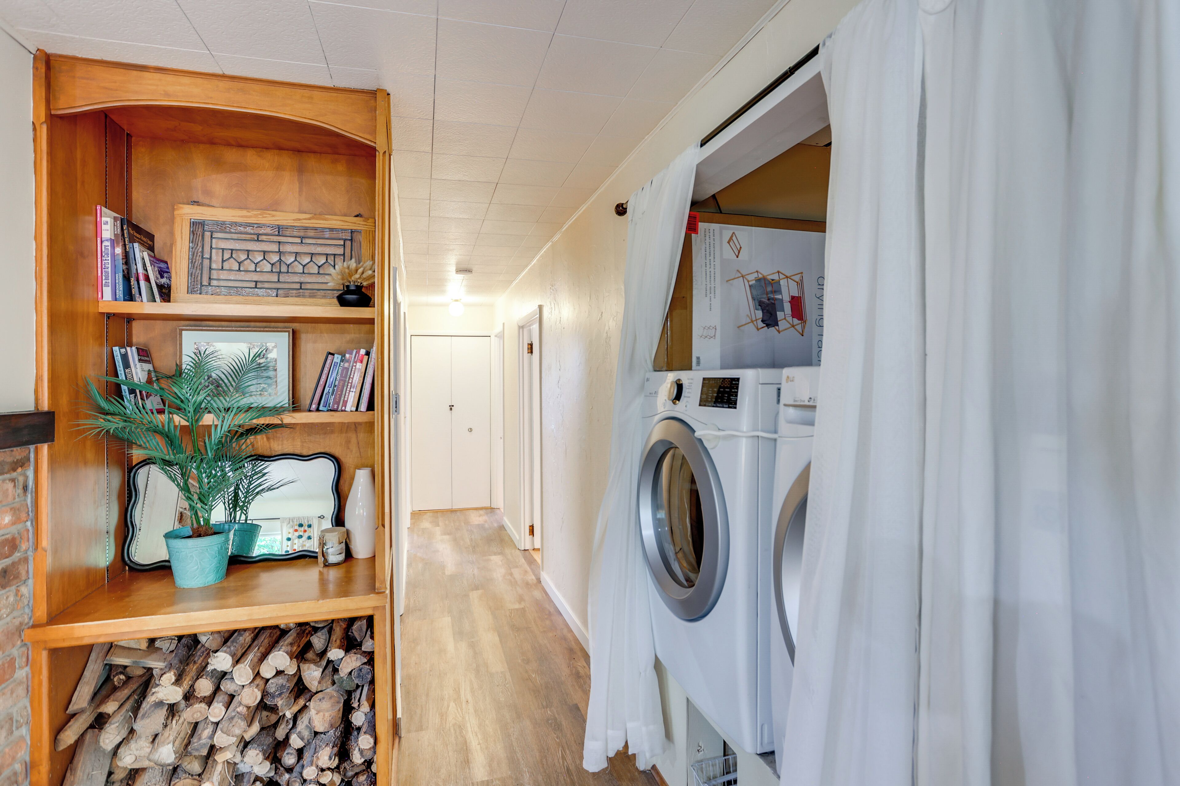 Une buanderie équipée d’un lave-linge, d’une étagère en bois avec des livres et une plante, et d’une porte donnant sur une autre pièce.