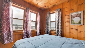 A room with a bed, wooden walls, and windows with patterned curtains. - Free Boat Rentals! Beachside Les Cheneaux Cabin (Cedarville)