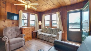 A cabin interior with a wooden ceiling, a ceiling fan, a television mounted on the wall, a sofa, a loveseat, and a wooden dresser. - Free Boat Rentals! Beachside Les Cheneaux Cabin (Cedarville)