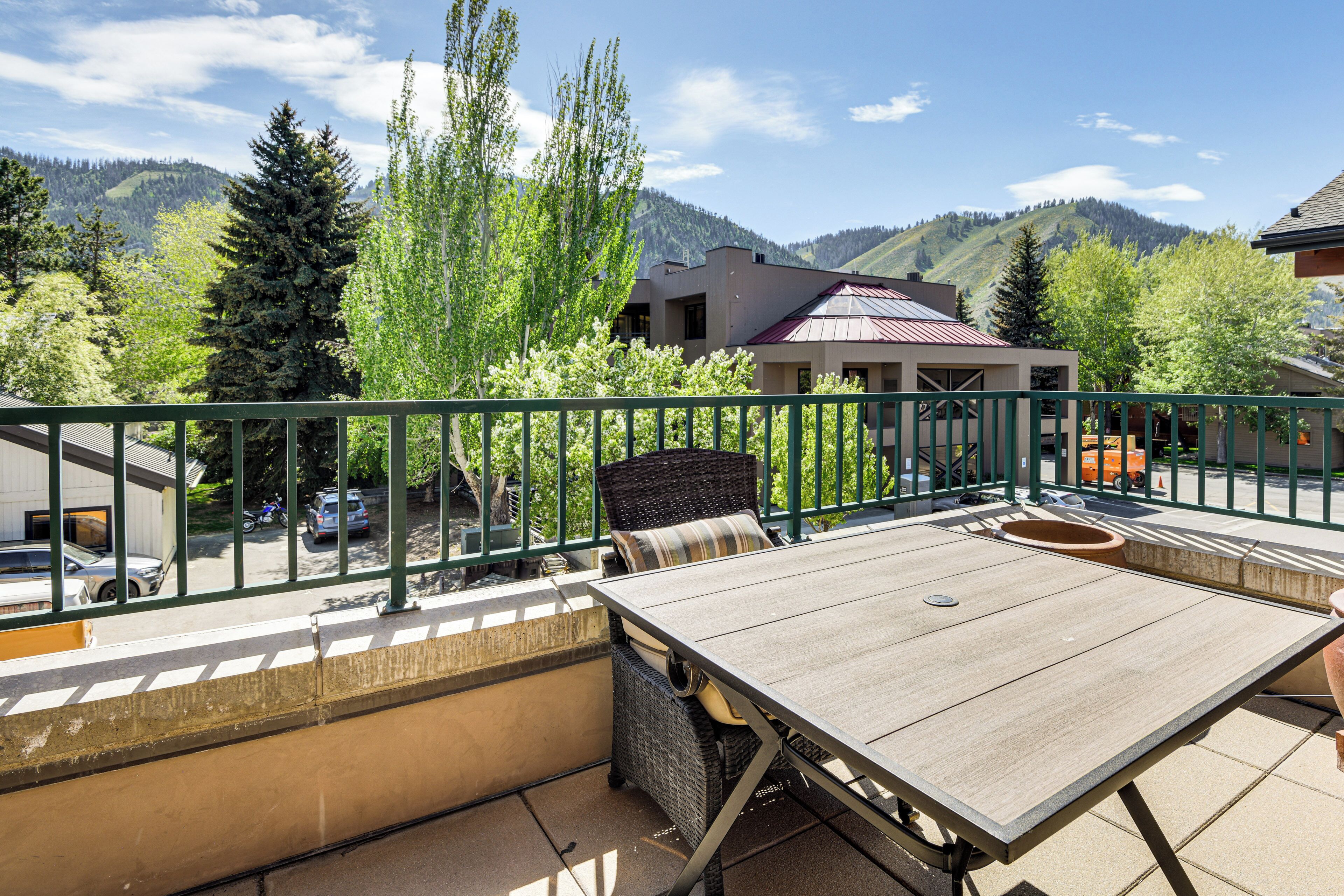 A balcony with a wooden table and chairs, overlooking a mountainous landscape with trees and buildings.