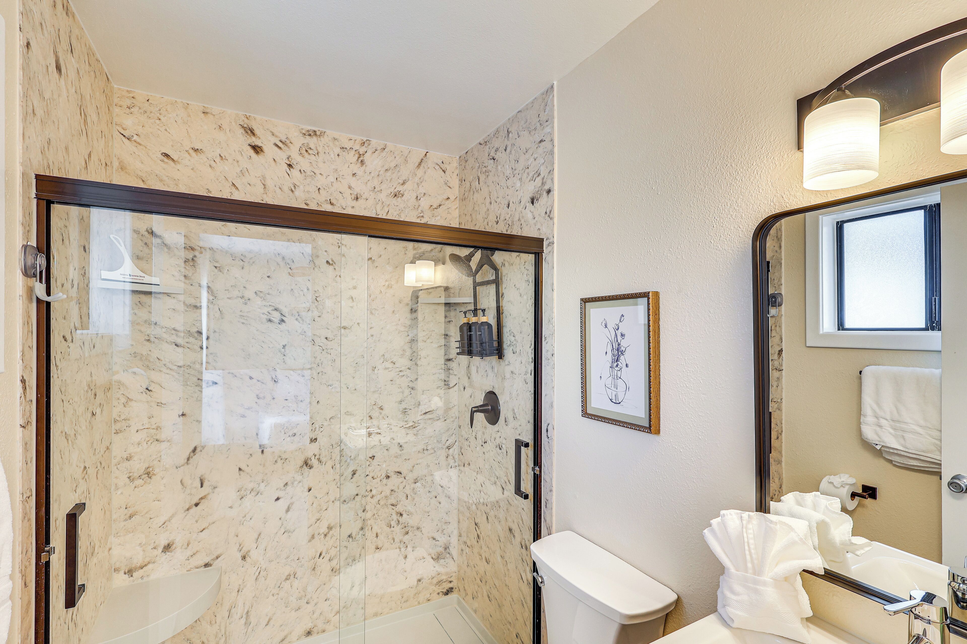 Un baño con ducha de vidrio, inodoro y lavamanos con espejo.