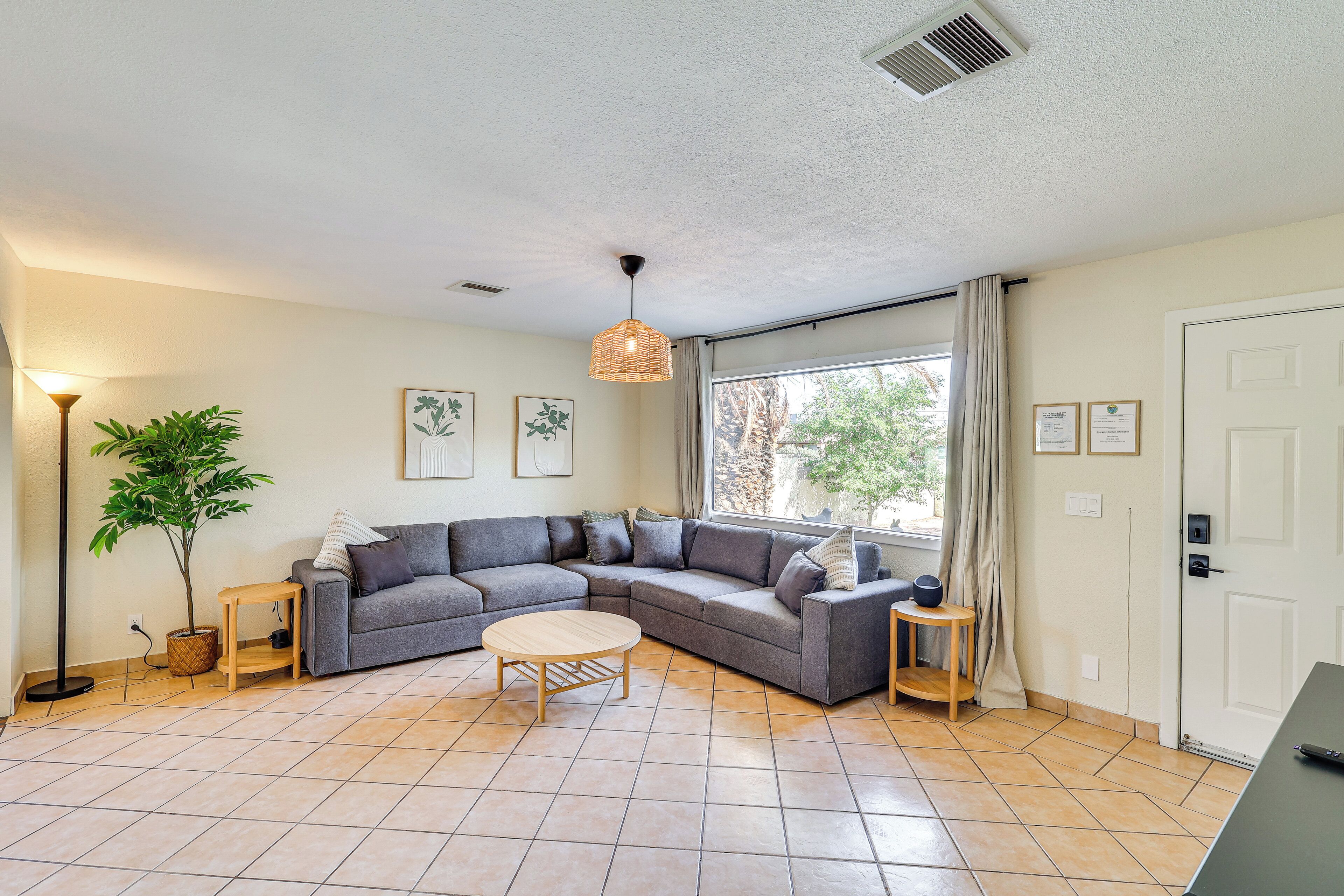 A living room with a grey sectional sofa, a round wooden coffee table, a floor lamp, and a potted plant.