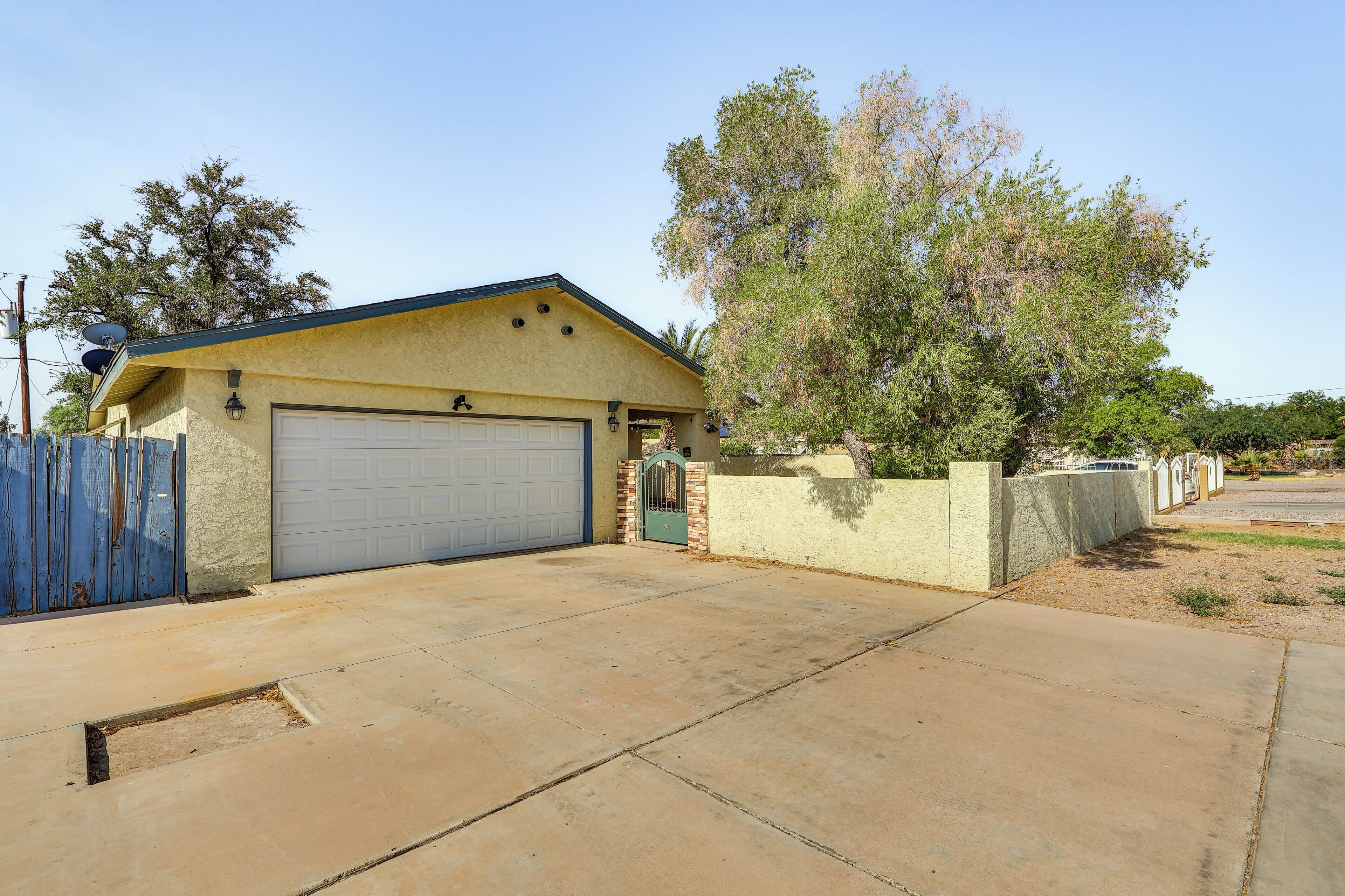 A single-story house with a garage, a blue gate, and a large tree in front.