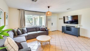 A living room with a sectional sofa, a round coffee table, a TV on a cabinet, and a large window with curtains. - Walk to Colorado River: Family Home w/ Yard! (Bullhead City)