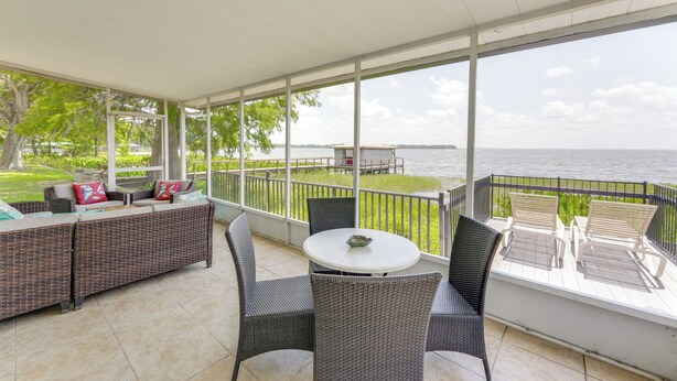 A covered patio with wicker furniture, a round table, and a view of the water. - Family Home w/ Stunning Water Views in Tavares! (Tavares)