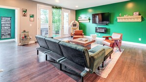 Un salon moderne avec un mur d’accent vert, un téléviseur à écran plat et un vieux juke-box.