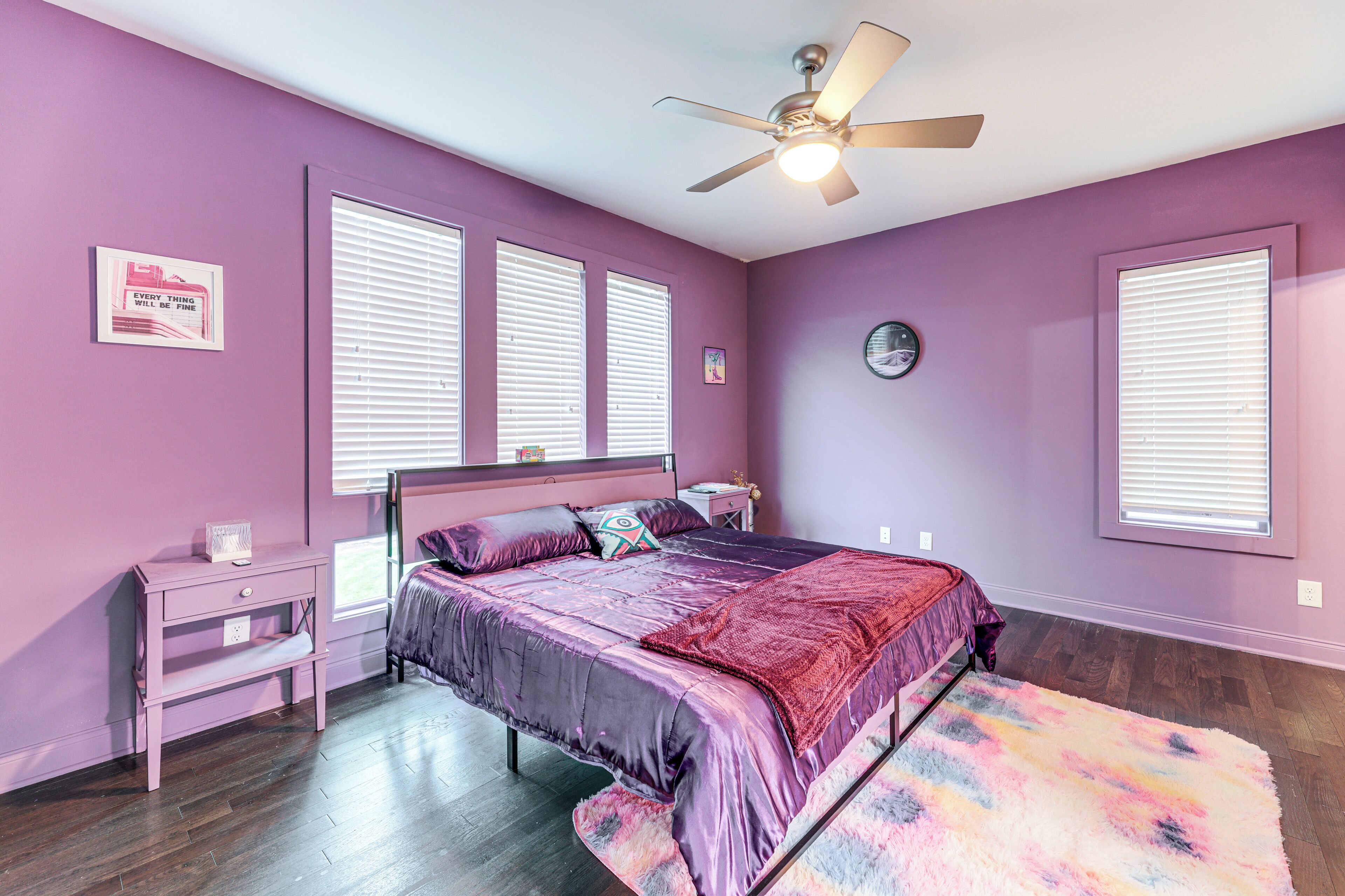 A bedroom with purple walls, a bed with a purple bedspread, a nightstand, a dresser, and a ceiling fan.