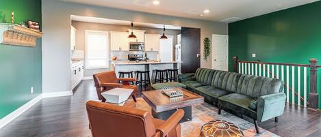 A modern living room with a sofa, coffee table, and chairs. There is a kitchen in the background with a microwave and refrigerator.
