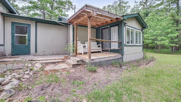 A wooden deck with a bench, a covered patio, and a stone pathway leading to a building with a green door and windows.
