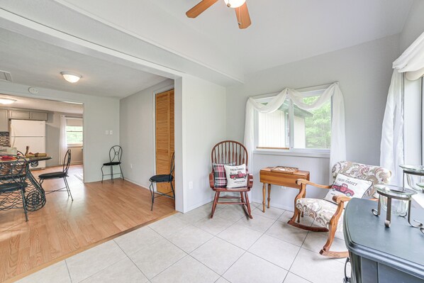 A spacious living room with a dining area, a kitchen in the background, and a large window with curtains.