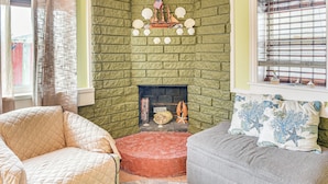 A cozy living room with a green brick fireplace, a comfortable beige armchair, and a gray sofa with decorative pillows.