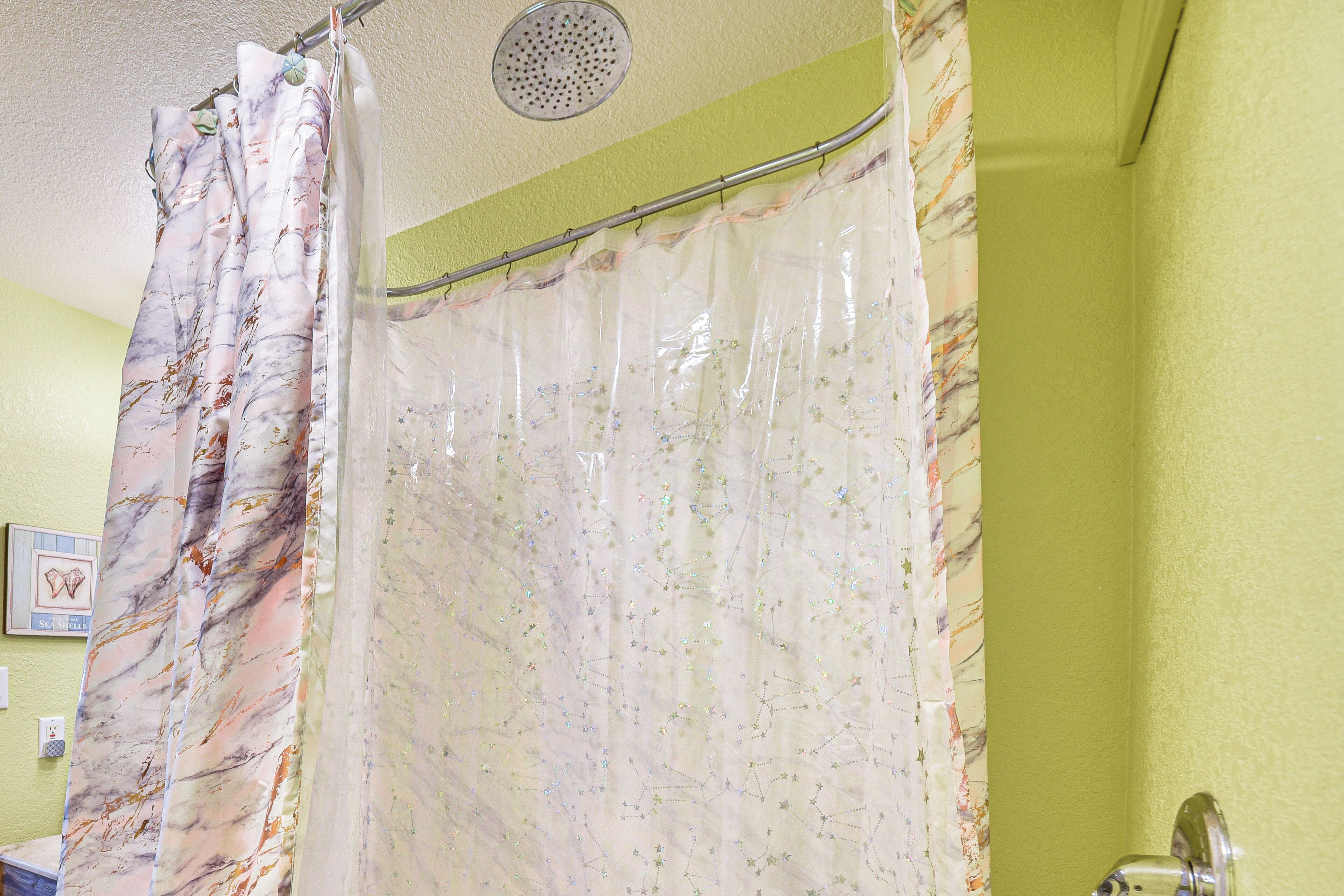 A bathroom with a shower curtain featuring a celestial pattern, a visible showerhead, and a light green wall.