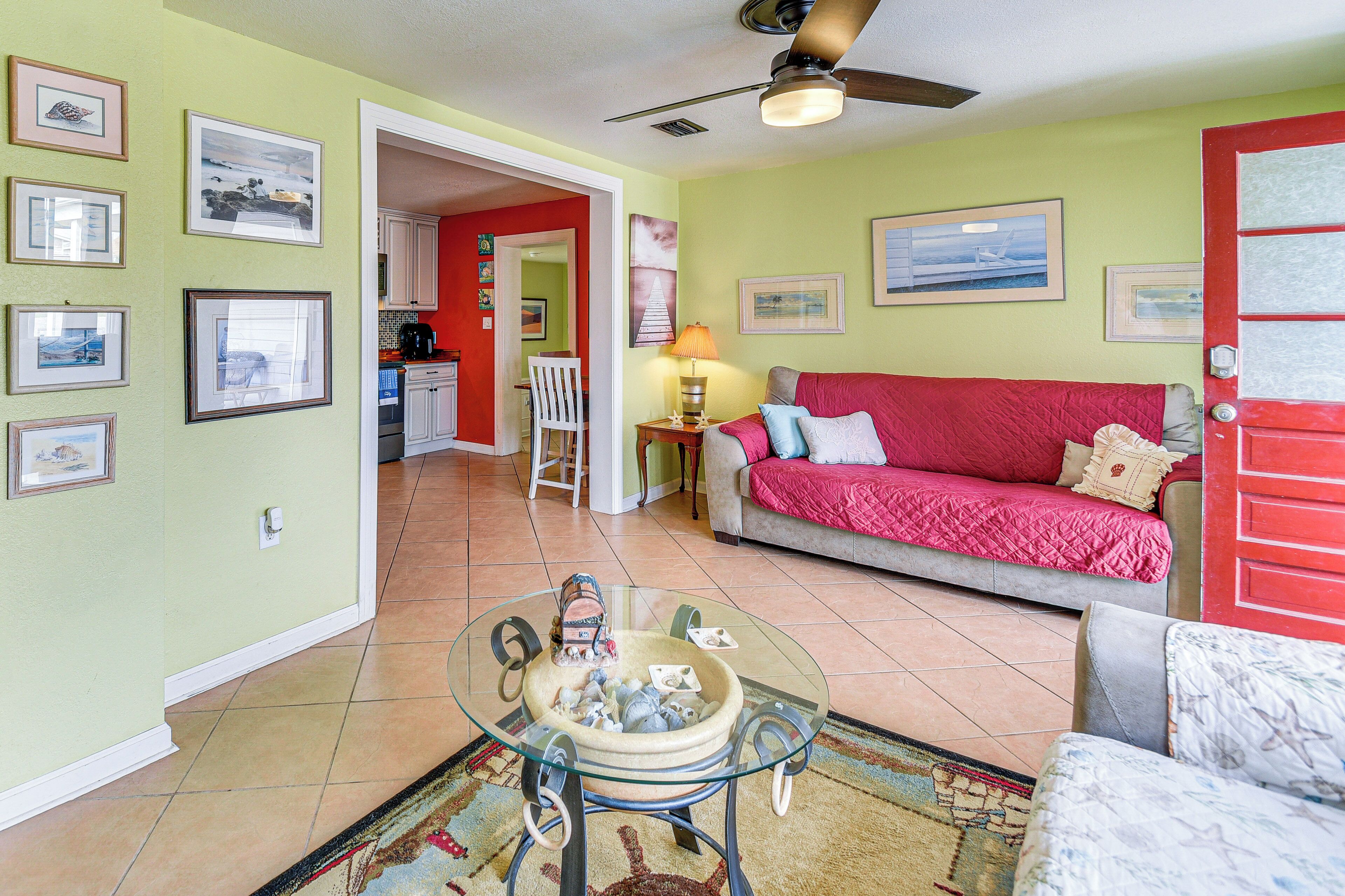 A living room with a glass coffee table, a red sofa, and a kitchen in the background.