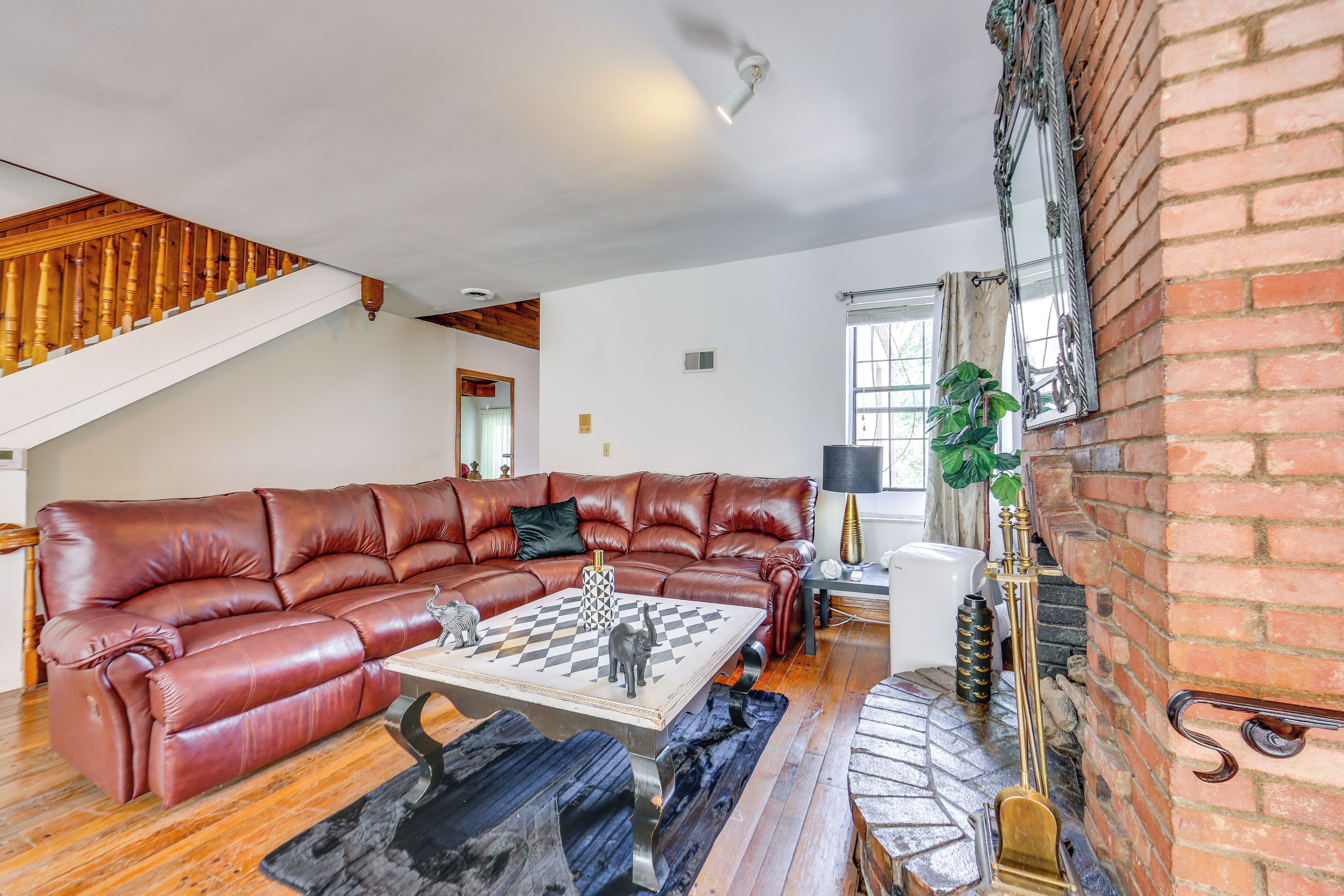 A spacious living room with a large leather sectional sofa, a coffee table with a chess set, and a fireplace with a brick wall.