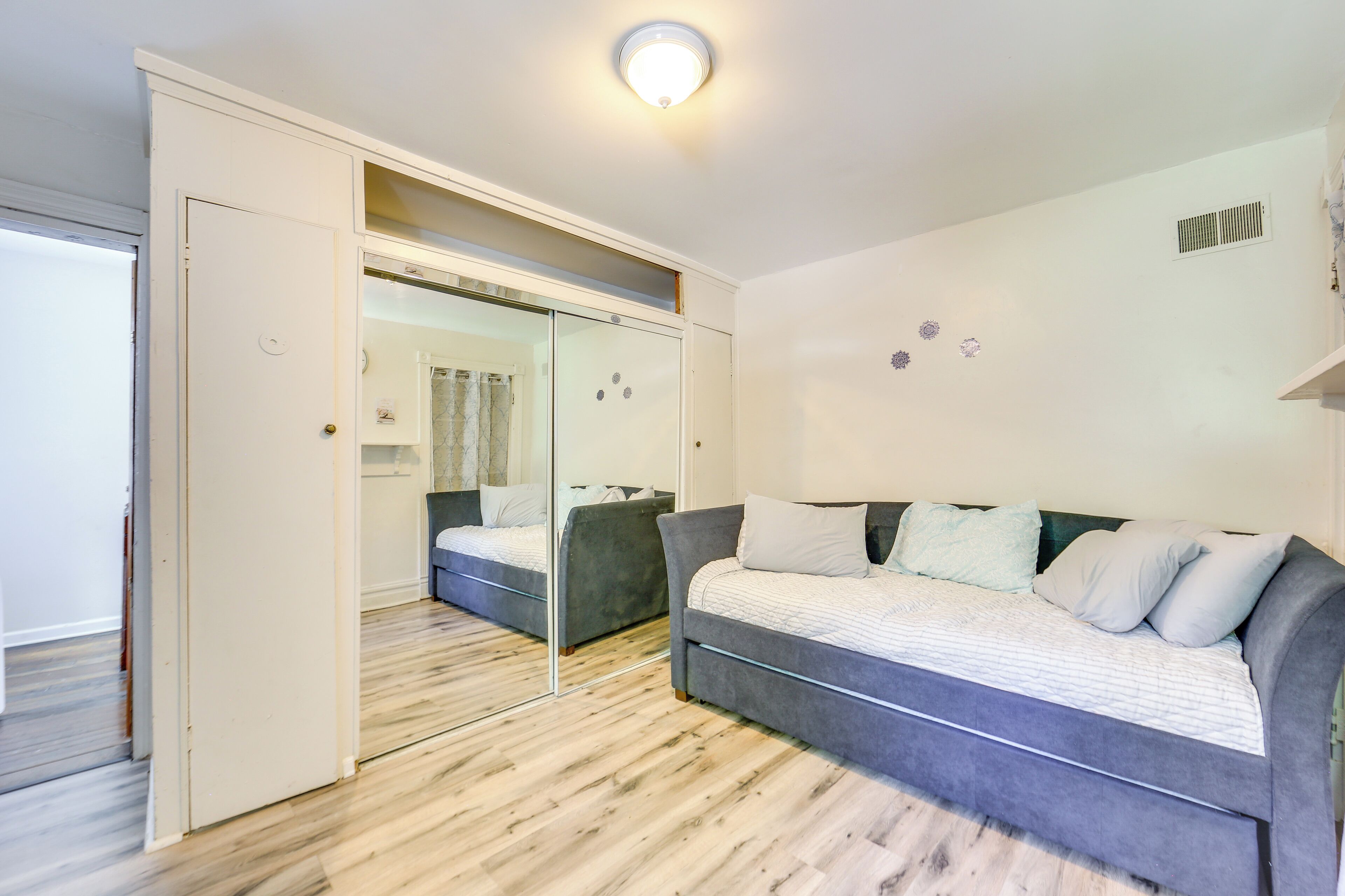 A modern bedroom with a grey sofa bed, a large mirror, and a wooden floor.