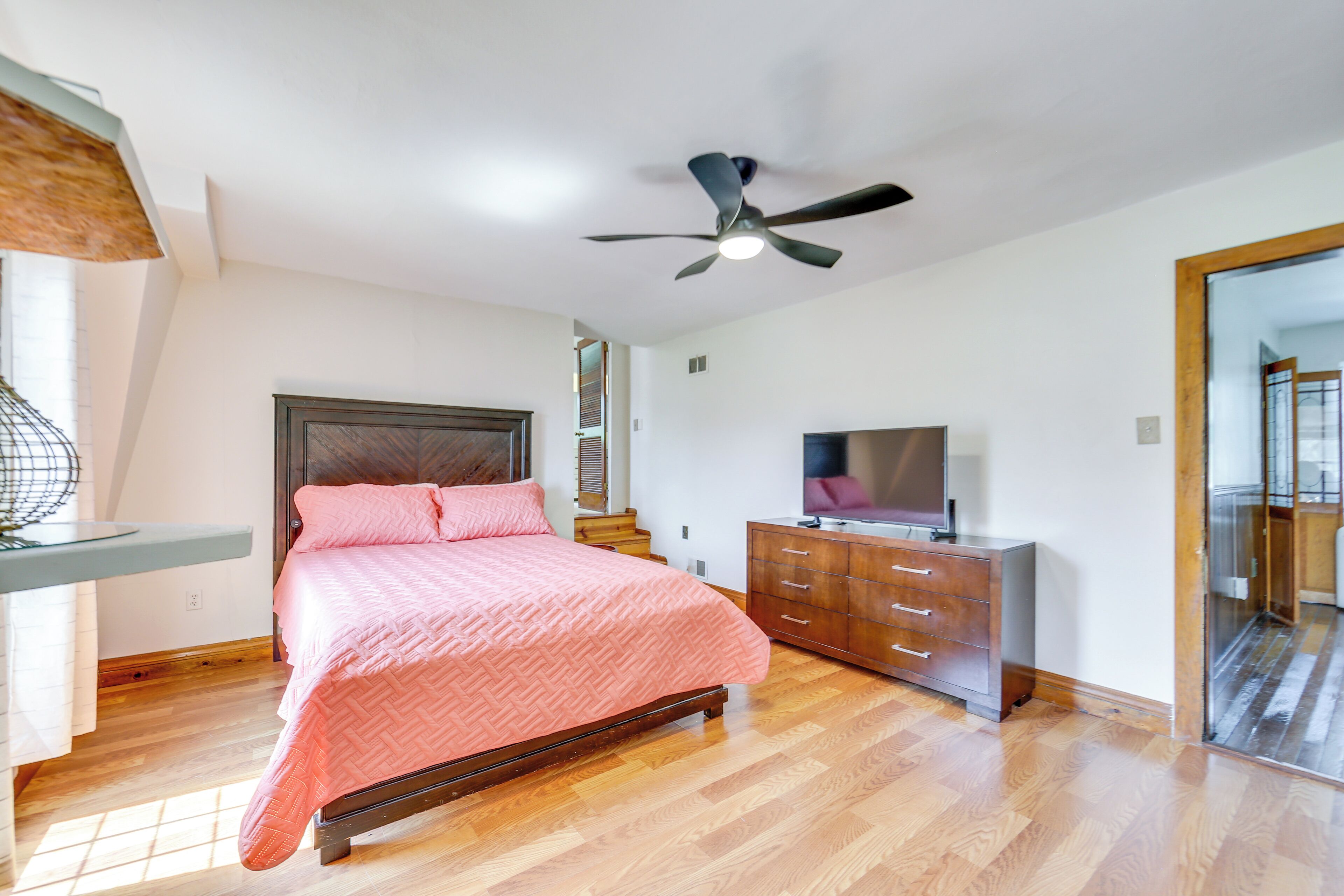 Un dormitorio con cama, cómoda, televisor y ventilador de techo.