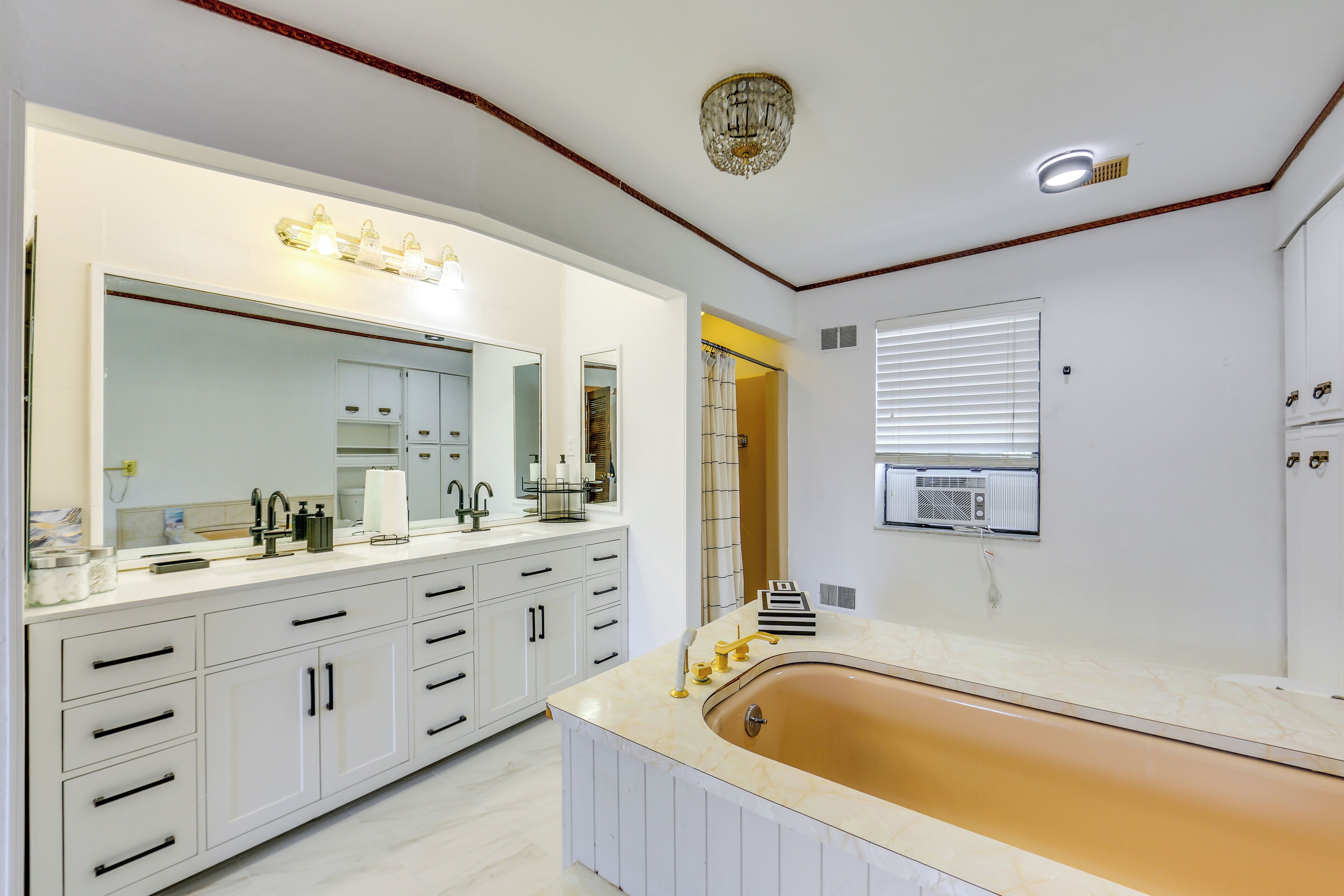 A modern bathroom with a large mirror, white cabinetry, a freestanding bathtub, and a ceiling light fixture.