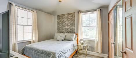 Une chambre à coucher avec un lit, une table de chevet, un ventilateur de plafond et une fenêtre avec des rideaux.