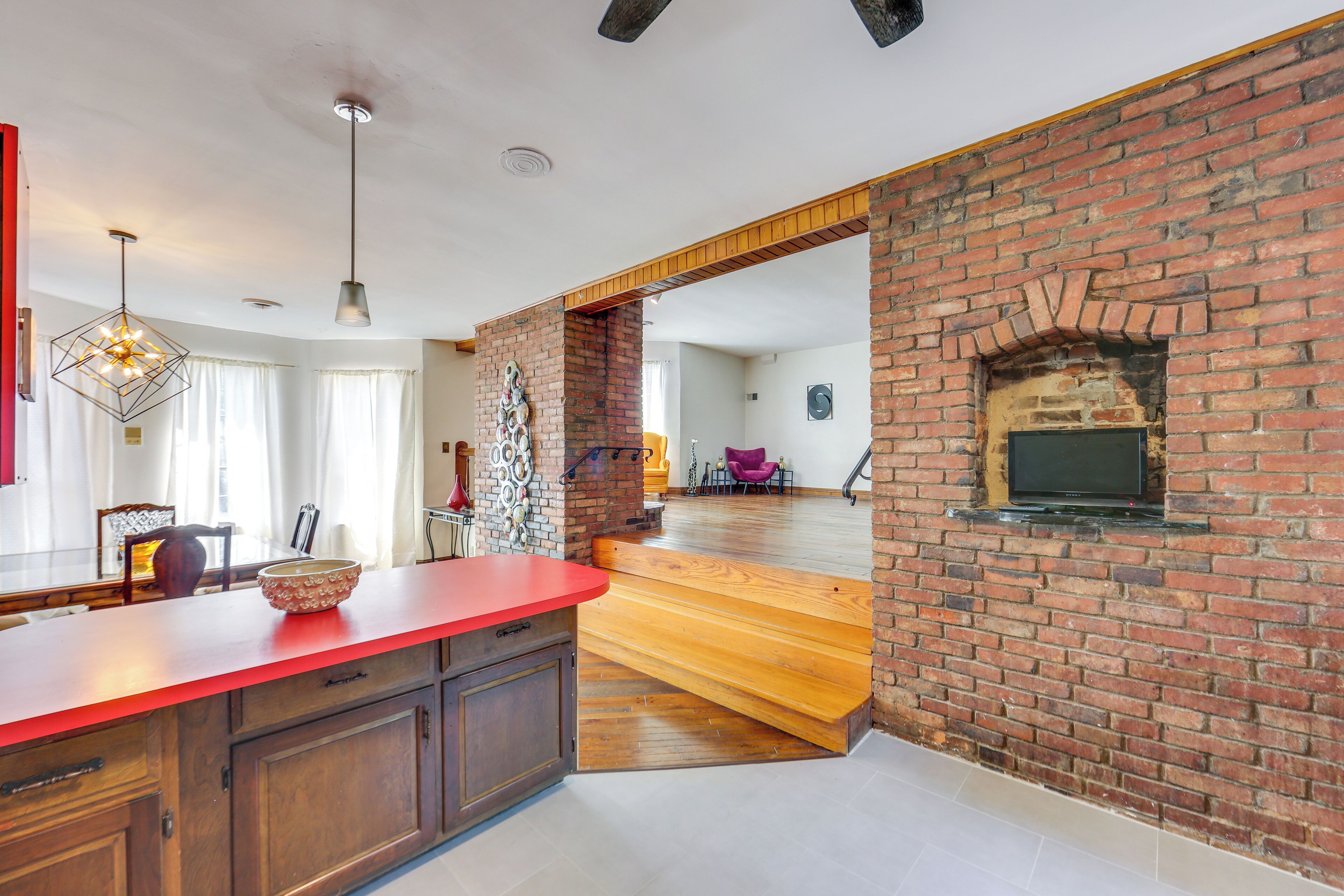 A spacious kitchen with a red countertop, wooden cabinets, and a brick wall with a fireplace.