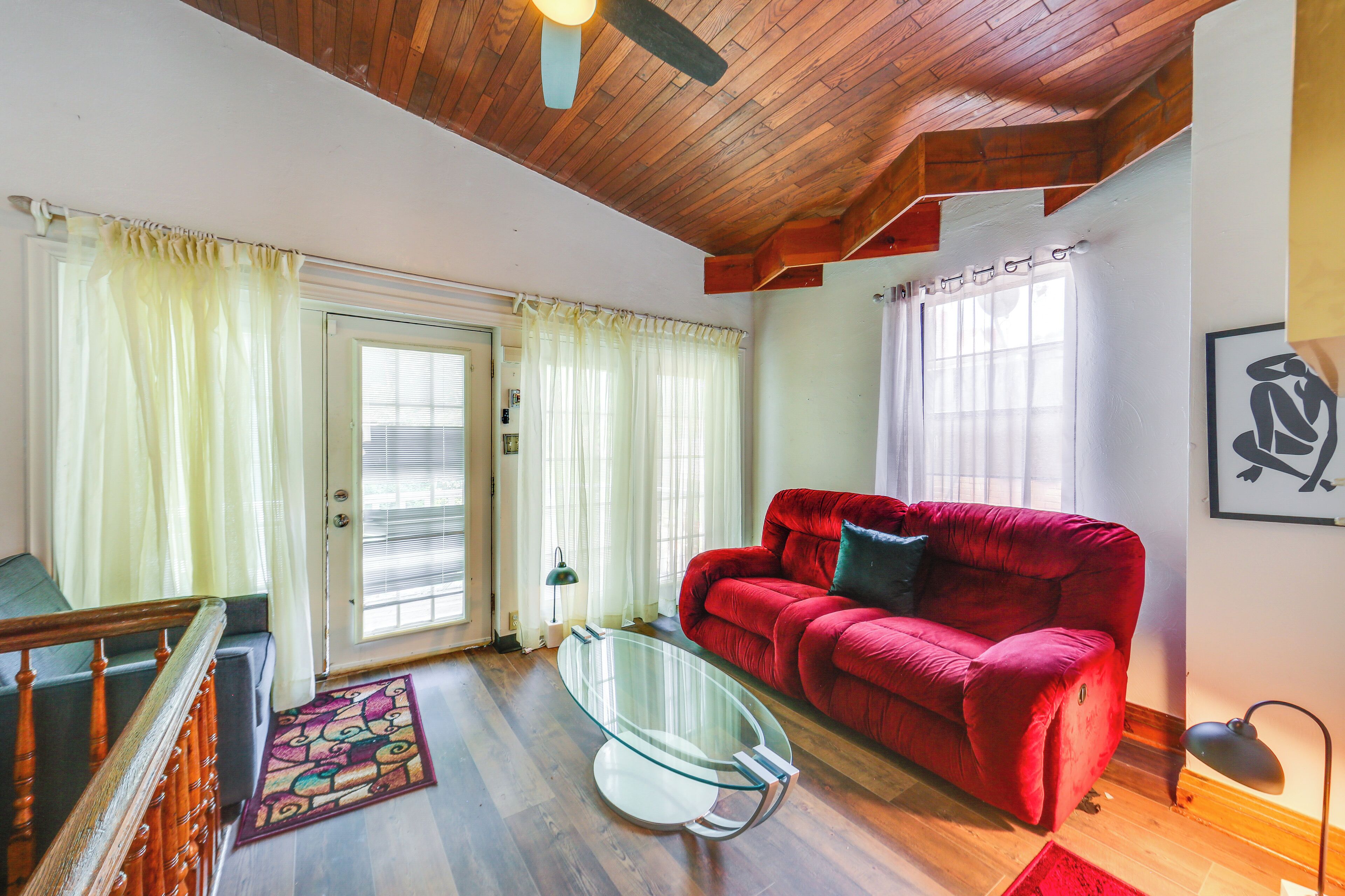 A living room with a red sofa, a glass coffee table, and a wooden ceiling.