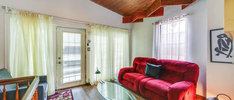 A living room with a red sofa, a glass coffee table, and a wooden ceiling.
