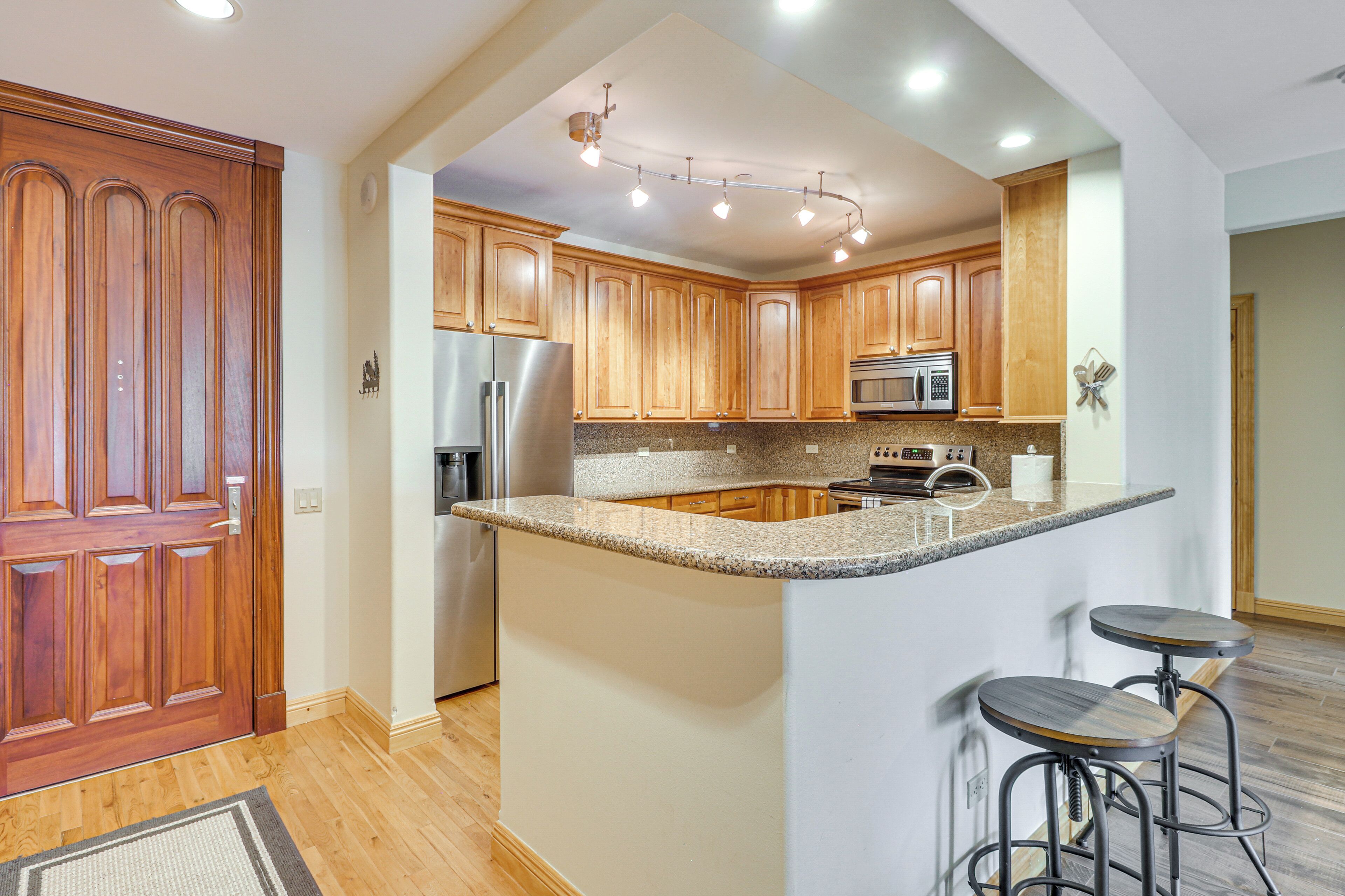 A kitchen with wooden cabinets, a stainless steel refrigerator, a microwave, and a granite countertop.