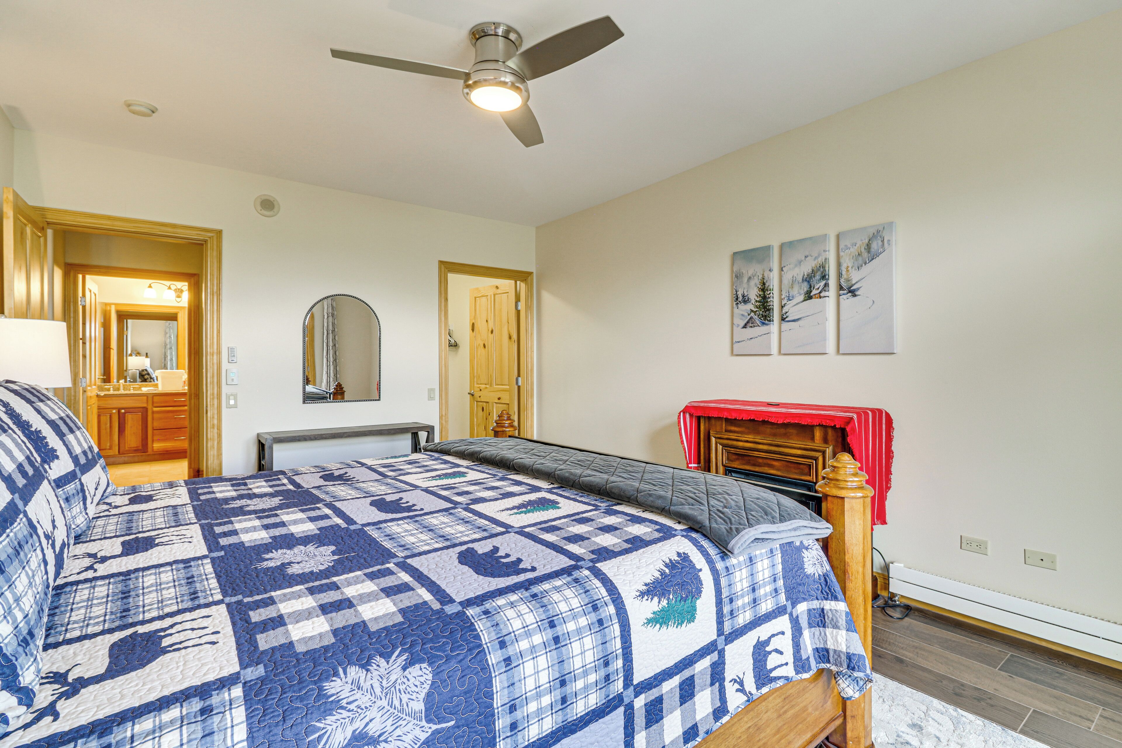 A bedroom with a bed, a ceiling fan, a wooden door, and a fireplace.