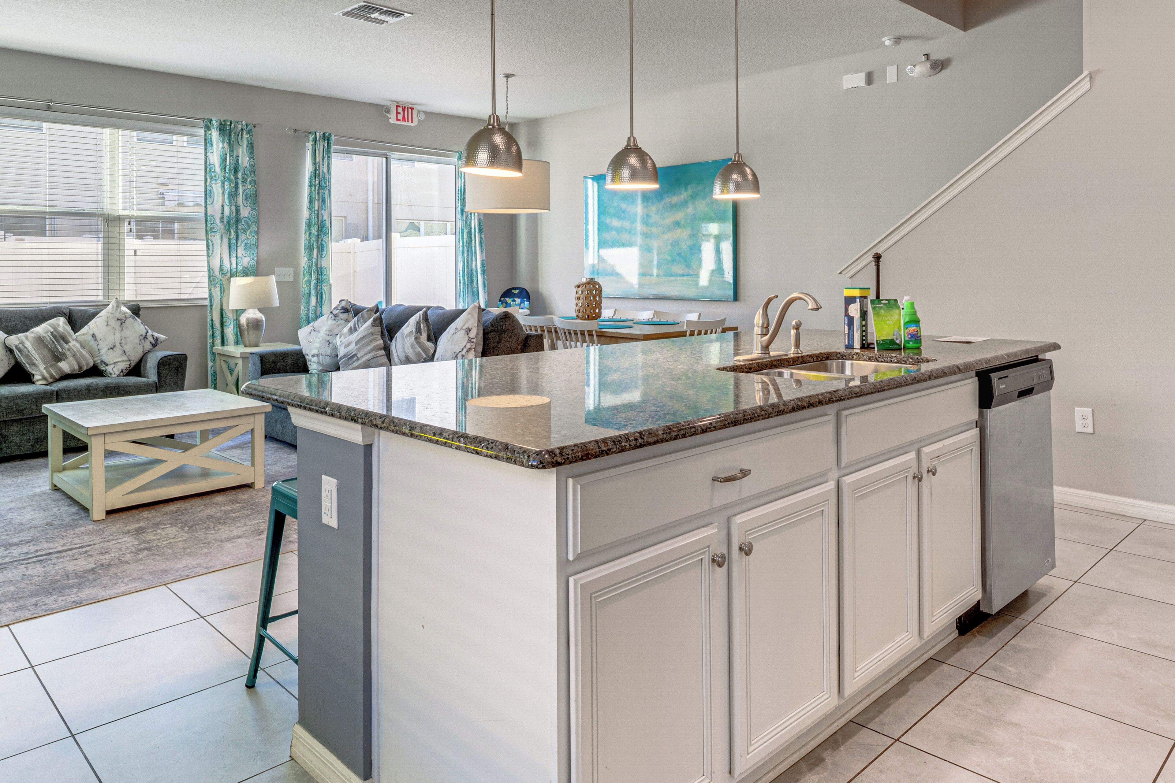 A modern kitchen with a central island, pendant lighting, and a dining area with a sofa and table.