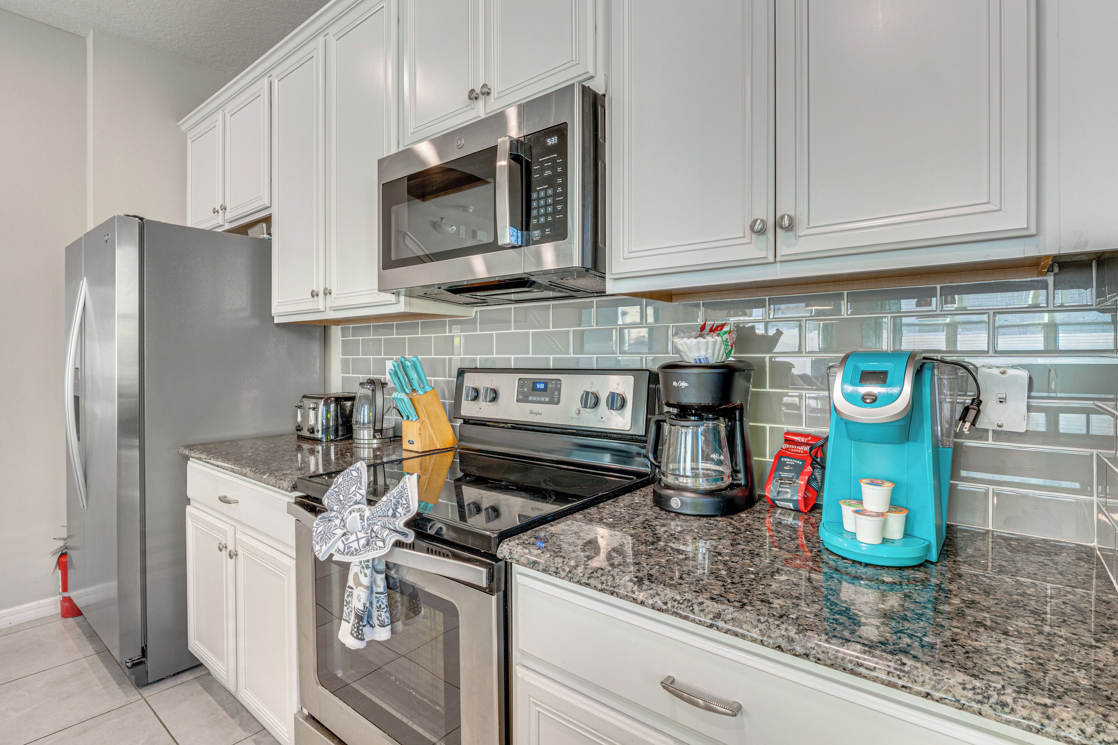 A modern kitchen with stainless steel appliances, white cabinetry, and a granite countertop.