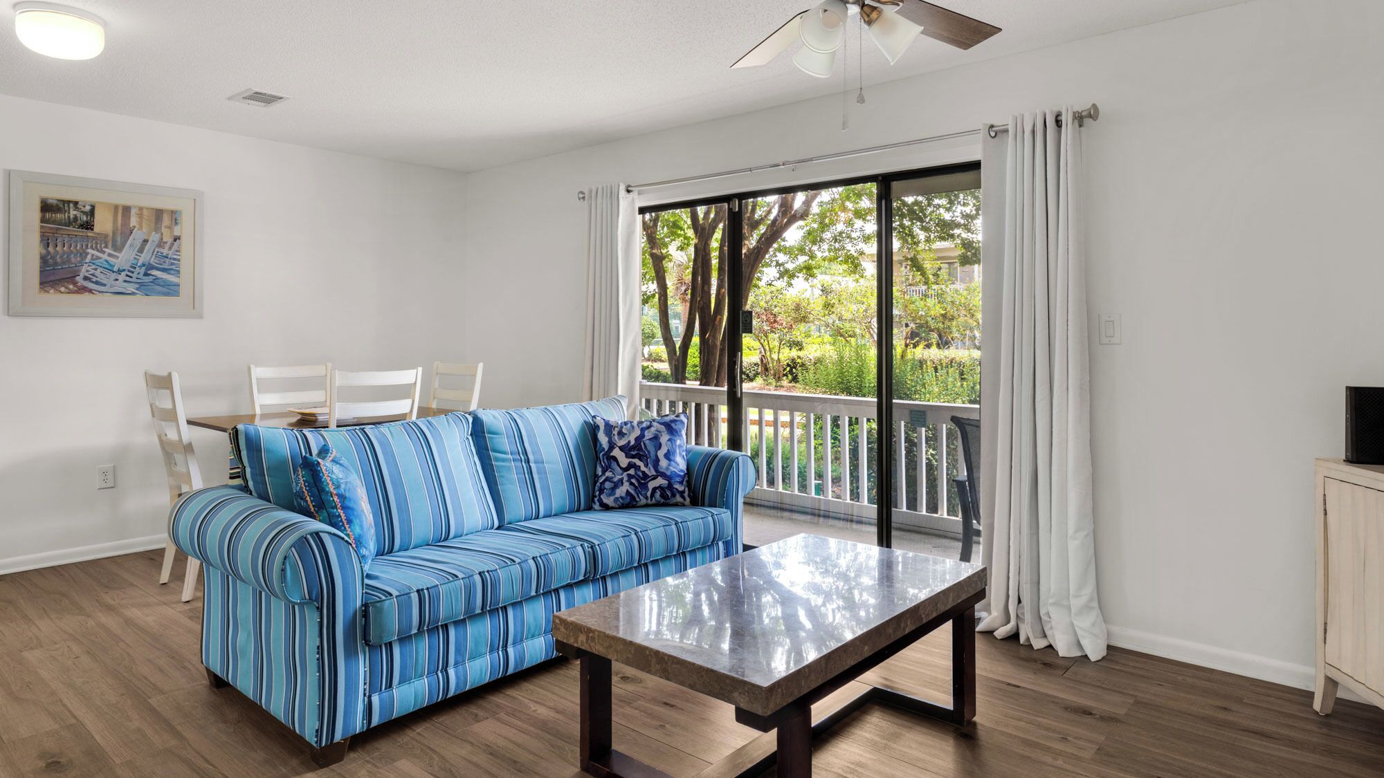 A living room with a striped sofa, a dining table, and a large window with curtains.