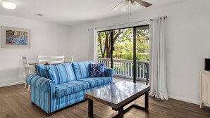 A living room with a striped sofa, a dining table, and a large window with curtains. - Minutes to Beach & Shops on 30A + Free tickets: Bikes, Dolphin Cruise & More! (Santa Rosa Beach)