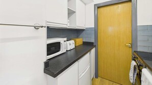 A compact kitchen with white cabinets, a microwave, a toaster, and a wooden door. - Host Stay Look Flat (Scarborough)
