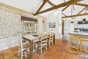 A rustic dining area with a stone wall, wooden beams, and a tiled floor. - Host Stay The Old Foundry (King's Lynn)