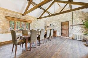 A rustic dining room with a stone wall, wooden beams, and a large window. - Host Stay The Old Foundry (King's Lynn)